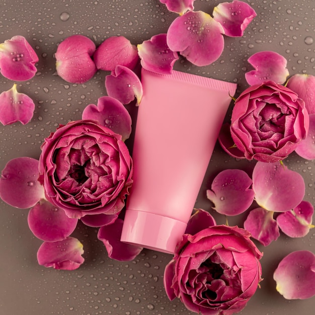Behälter für Hautpflegeprodukte auf hellrosa Hintergrund mit blühenden Rosenblüten. Nahansicht. Paketmodell ohne Markenzeichen