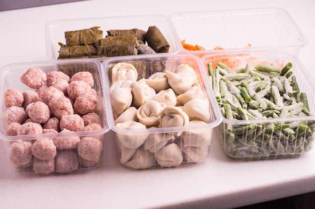 Behälter mit gefrorenem Gemüse und halbfertigen Fleischprodukten aus dem Kühlschrank. Frikadellen, Knödel, Dolma in Weinblättern, gehackte Bohnen und geriebene Karotten