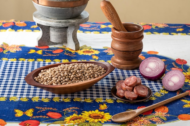 Behälter mit rohen Bohnen, geräucherter Wurst, einer roten Zwiebel aus Holzstößel und einem Steintopf, Zutaten für die Zubereitung eines brasilianischen Bohnenrezepts