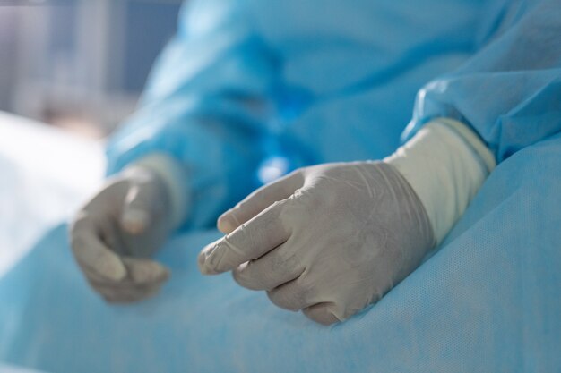 Behandschuhte Hände eines müden professionellen Chirurgen, der in der Pause im Operationssaal sitzt und sich vor der nächsten medizinischen Operation in Kliniken ausruht