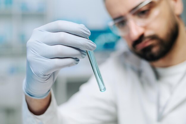 Foto behandschuhte hand eines jungen männlichen wissenschaftlers, der eine flasche mit blauer flüssigkeit hält