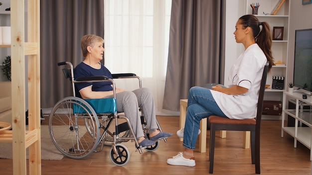 Behinderte ältere Frau im Rollstuhl im Gespräch mit Arzt. Altenheim, Gesundheitspflege, Gesundheitshilfe, Sozialhilfe, Arzt- und Heimservice