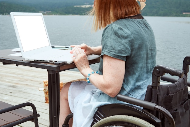 Behinderte gesichtslose Frau benutzt Laptop im Freien. Fernarbeit, Lernkonzept.