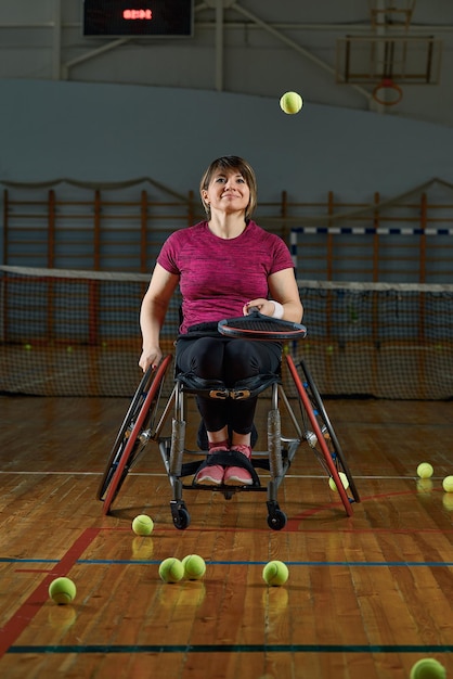 Behinderte junge Frau auf dem Rollstuhl, der Tennis auf Tennisplatz spielt