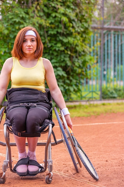 Behinderte junge Frau im Rollstuhl, die auf dem Tennisplatz Tennis spielt