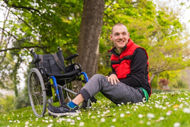 Behinderte Person in einem öffentlichen Stadtpark, die in einem Rollstuhl sitzt und lächelnd auf dem Gras mit den Frühlingsblumen sitzt