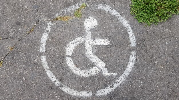 Behindertenparksymbol. Behindertenbucht markiert mit einer Person in einem Rollstuhlschild auf grauem Asphalt auf einem großen Parkplatz aus nächster Nähe. von oben betrachten.