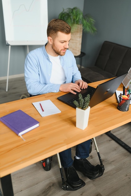 Behinderter Geschäftsmann sitzt im Rollstuhl mit Computer am Arbeitsplatz