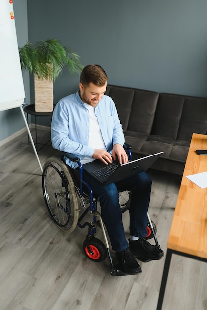 Behinderter Geschäftsmann sitzt im Rollstuhl mit Computer am Arbeitsplatz