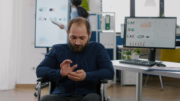 Behinderter junger Mitarbeiter, der während der Arbeitszeit auf dem Handy sucht