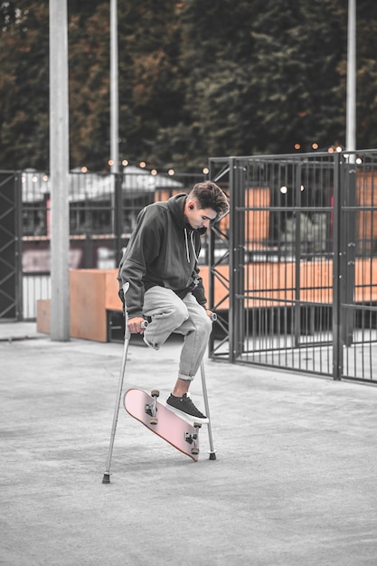 Foto behinderter kerl auf krücken, der trick mit skateboard macht