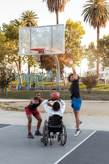 Behinderter Mann im Rollstuhl, der Basketball mit Leuten spielt