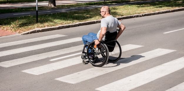 Behinderter Mann im Rollstuhl, der Straßenstraße kreuzt.