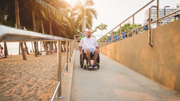 Behinderter Mann im Rollstuhl fährt auf einer Rampe zum Strand.