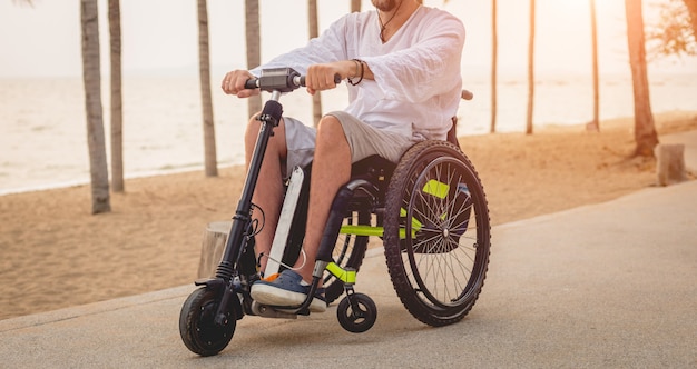 Behinderter Mann im Rollstuhl mit Elektroroller am Strand