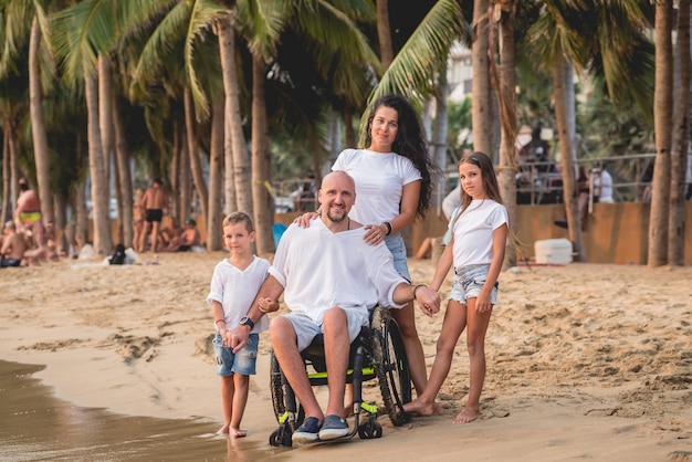 Behinderter Mann im Rollstuhl mit seiner Familie am Strand.