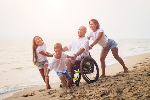 Behinderter Mann im Rollstuhl mit seiner Familie am Strand.