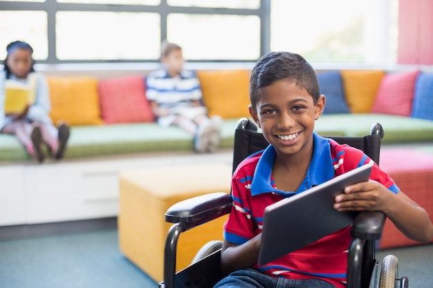 Behinderter Schüler auf Rollstuhl unter Verwendung der digitalen Tablette in der Bibliothek