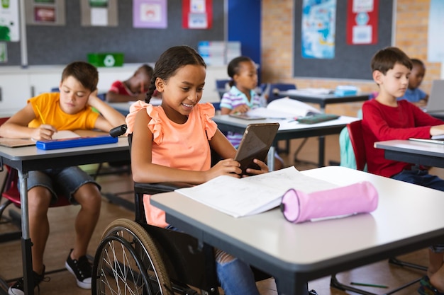 Behindertes afroamerikanisches Mädchen nutzt digitales Tablet, während es in der Grundschule im Rollstuhl sitzt