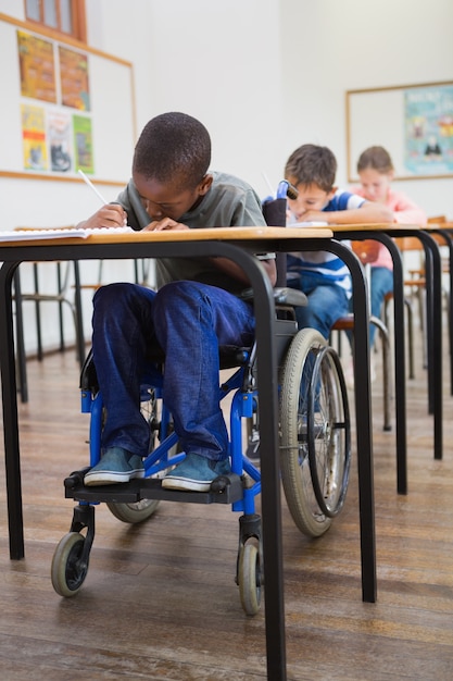 Behindertes Schülerschreiben am Schreibtisch im Klassenzimmer