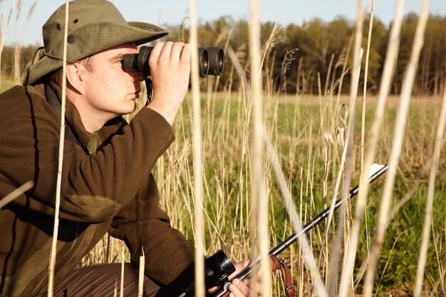 Foto bei näherer betrachtung ein mann in der wildnis, der durch sein fernglas schaut und sein gewehr hält