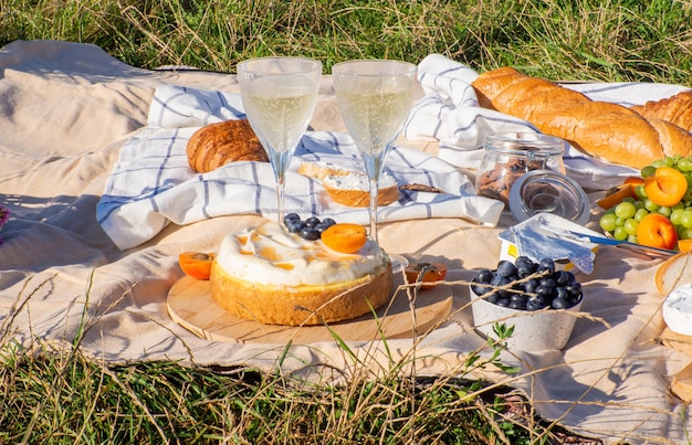 Beige Decke mit Obst und Gebäck, Kekse, Beeren, Käse und Baguette. Konzept für ein Picknick für zwei in einem Stadtpark während Sommerferien oder Wochenenden. Kopierplatz. Zwei Gläser Wein.