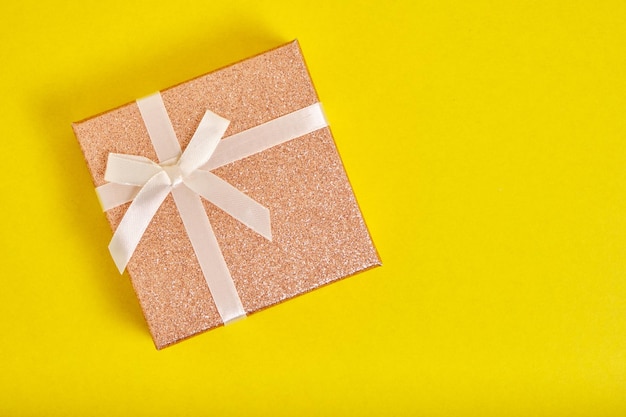 Beige Geschenkbox ist mit Band mit Schleife auf gelbem Hintergrund gebunden