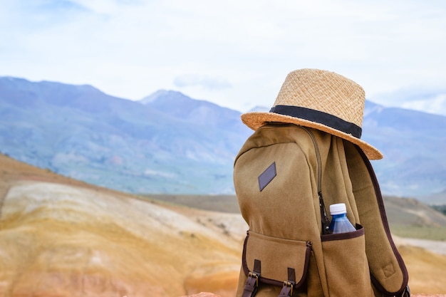 Beige Rucksack, Wasserflasche und Strohhut oben auf dem Berg. Aktives Reisekonzept.