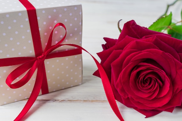 Beige Tupfengeschenkbox mit rotem Bandbogen und bautiful roten Rosen auf hölzernem Hintergrund. Grußkarte für Urlaub.