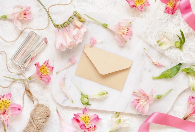 Beige Umschlag auf einem weißen Tisch zwischen rosa Blumen Draufsicht