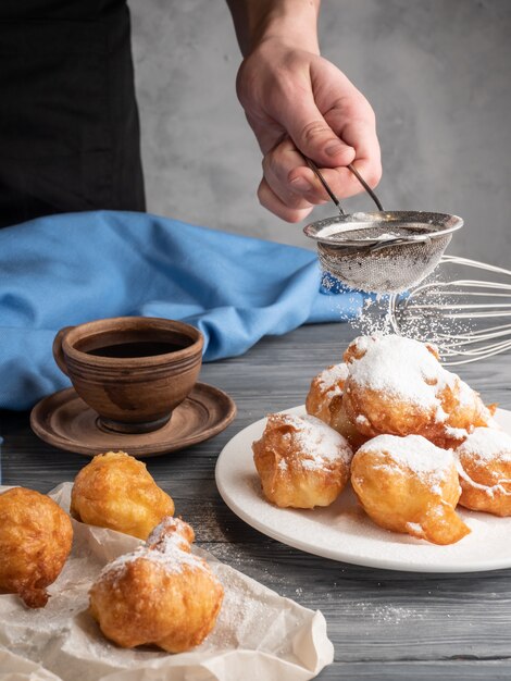 Beignet espolvoreado con azúcar glas sobre una mesa de madera con café y leche.