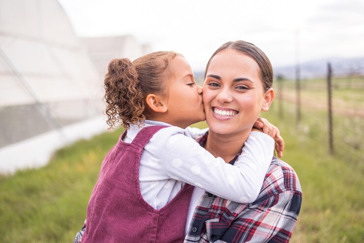 Foto beijo de mãe e menina em uma fazenda de agricultura e ecologia de sustentabilidade com amor e carinho familiar retrato de uma mãe e filho em uma energia limpa ecológica e campo de agricultura verde com sorriso