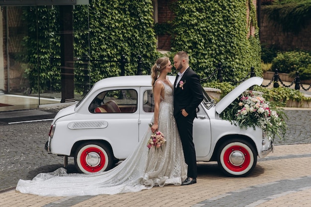 Beijo sensual dos dois no dia do casamento perto de carro retrô com flores