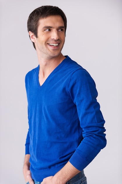 Beiläufig gutaussehend. Seitenansicht eines gutaussehenden jungen Mannes im blauen Pullover, der über die Schulter schaut und lächelt
