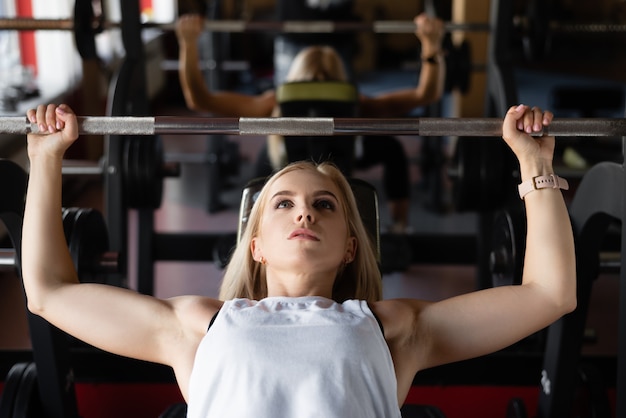 Beim Training im Fitnessstudio ist ein junges schönes Mädchen auf einer Bank beschäftigt und macht Bankdrücken. Aktiver Lebensstil