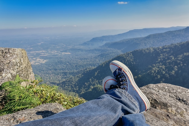 Bein eines Mannes, der am Rand einer Klippe an den Bergen, Wanderer sich entspannt auf Klippe sitzt