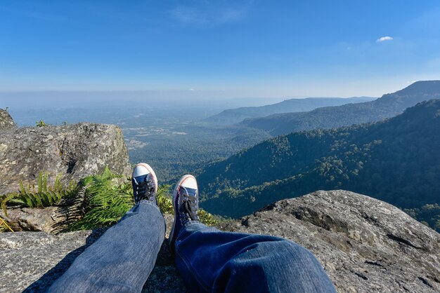 Bein eines Mannes, der am Rand einer Klippe an den Bergen, Wanderer sich entspannt auf Klippe sitzt