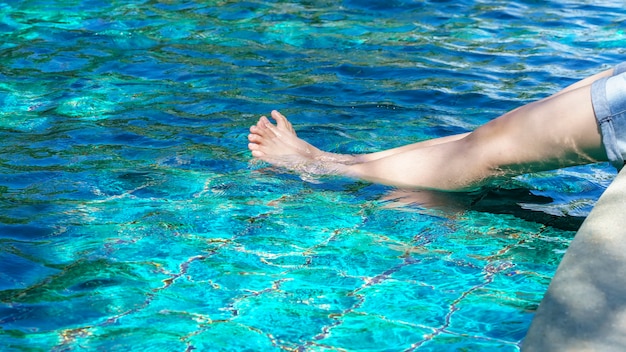 Beine des asiatischen Jugendlichen entspannend am Swimmingpool