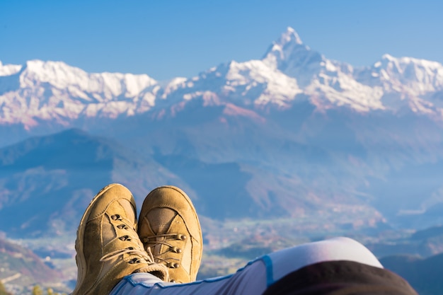 Beine des Reisenden in Wanderschuhen, die auf einer hohen Bergklippe sitzen und den Landschaftsberg genießen. Reise-, Freiheits-, Trekking- und Wanderkonzept. Stock Foto