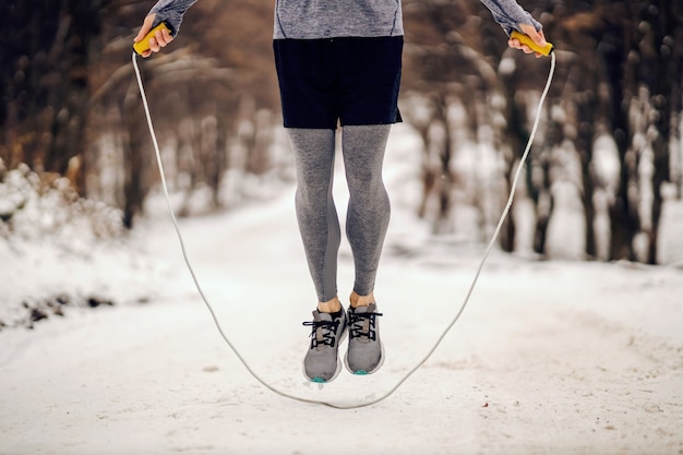 Beine, die im Winter das Seil auf schneebedecktem Weg springen. Wintersport, Cardio-Übungen, gesunde Gewohnheiten