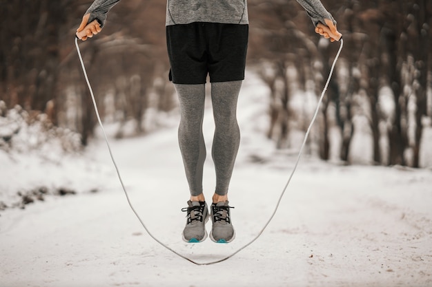 Beine, die im Winter das Seil auf verschneiten Pfaden springen. Wintersport, Cardio-Übungen, gesunde Gewohnheiten