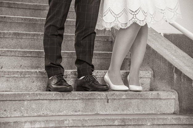 Foto beine eines hochzeitspaares, schuhe einer braut und eines bräutigams, die in schwarz-weiß auf einer treppe stehen