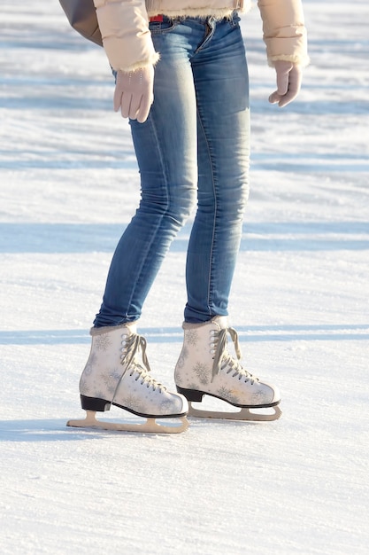 Beine eines Mädchens in Blue Jeans und weißen Schlittschuhen auf einer Eisbahn