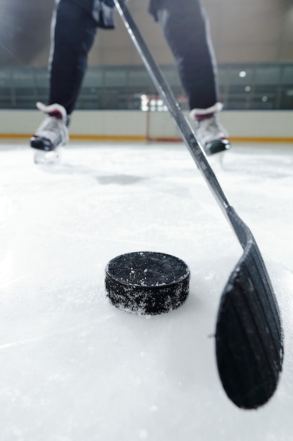 Beine eines männlichen hockeyspielers in sportuniform und schlittschuhen, die auf der eisbahn gegen die stadionumgebung stehen, während sie puck schießen