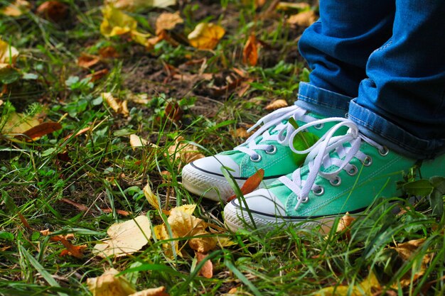 Beine in Blue Jeans und trendigen Turnschuhen auf dem Gras mit Herbstlaub