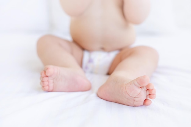 Beine oder Füße eines sechs Monate alten Babys in Nahaufnahme auf einem weißen Baumwollbett zu Hause