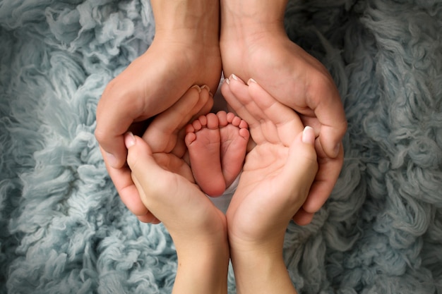 Beine und Zehen eines Neugeborenen. Eltern halten die Beine des Neugeborenen in ihren Handflächen. Die Handflächen des Vaters und der Mutter. Foto in hoher Qualität