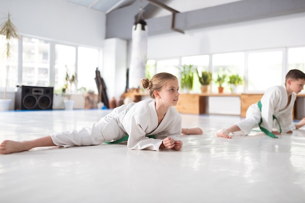 Beinspaltung machen. Ansprechendes aktives Mädchen mit Haarknoten, das das Bein spaltet, bevor es Aikido praktiziert