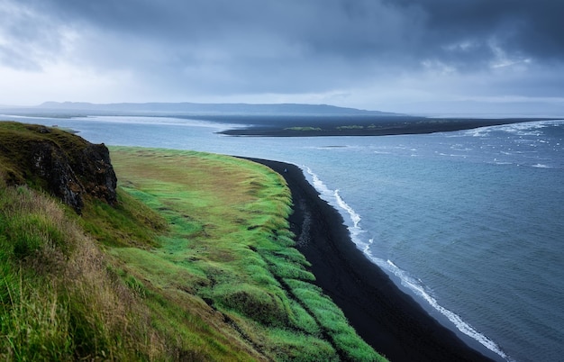 Beira-mar na Islândia Pedras altas e grama na hora do dia perto do mar Paisagem natural no verão Imagem de viagem islandesa