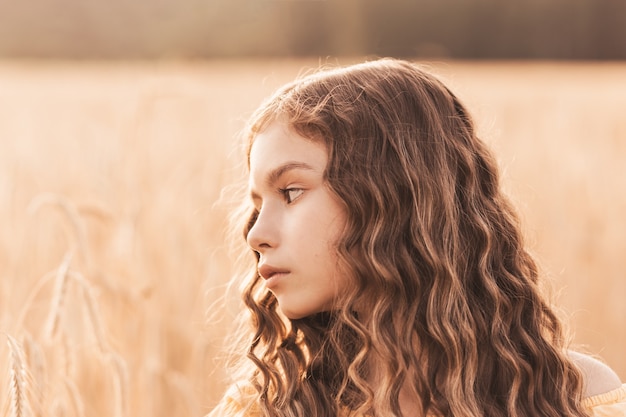 Bela adolescente com cabelo comprido, caminhando por um campo de trigo em um dia ensolarado. Retrato ao ar livre. Colegial relaxando